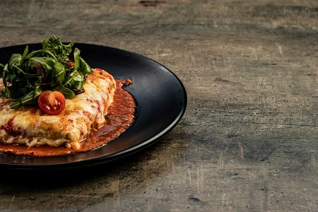 Na czarnym talerzu leży zapieczony makaron cannelloni z sosem pomidorowym